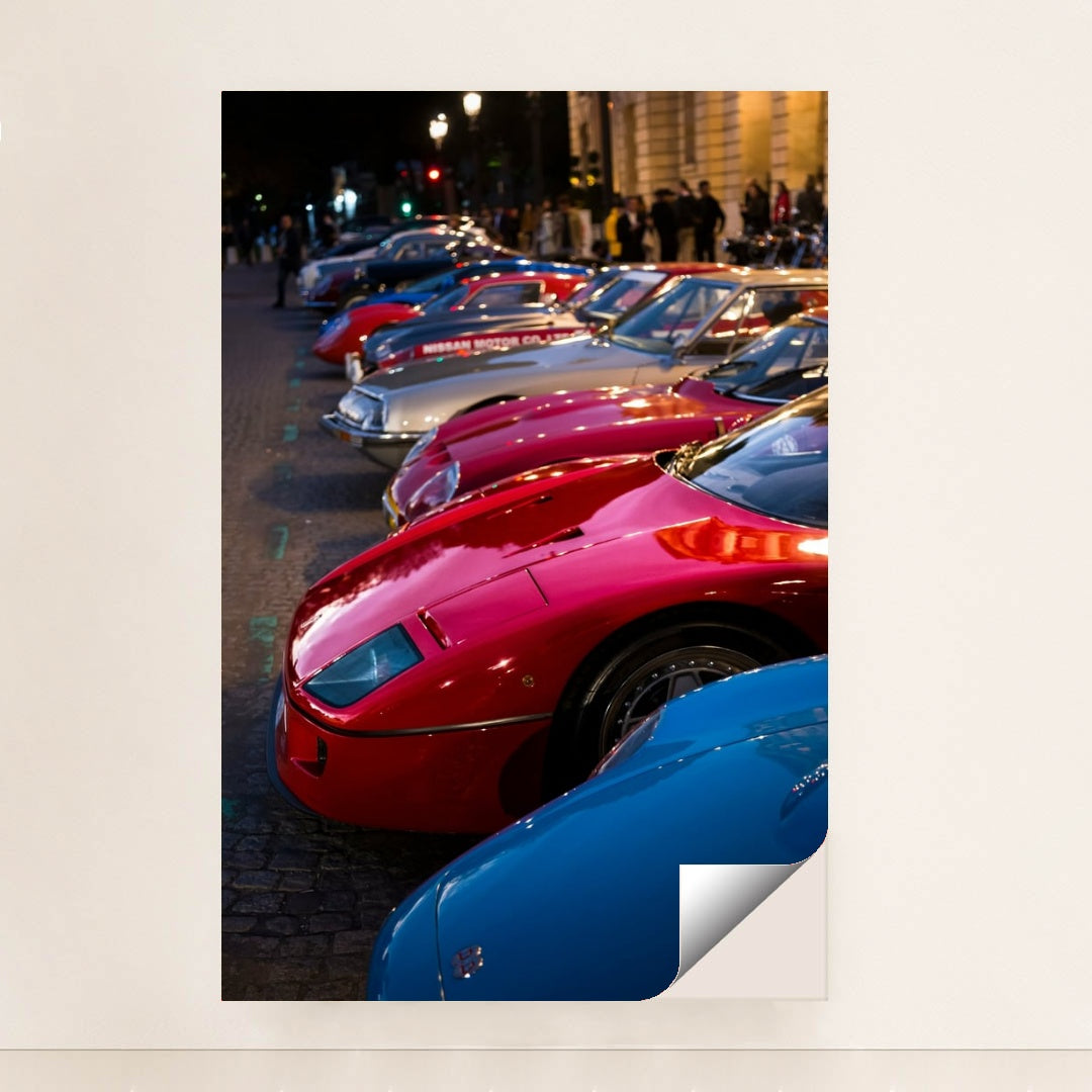 This photo shows a row of vintage sports cars, including a red Ferrari F40, parked on a cobblestone street at dusk, minimalist unframed style.