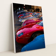 This photo shows a row of vintage sports cars, including a red Ferrari F40, parked on a cobblestone street at dusk, in a white frame.