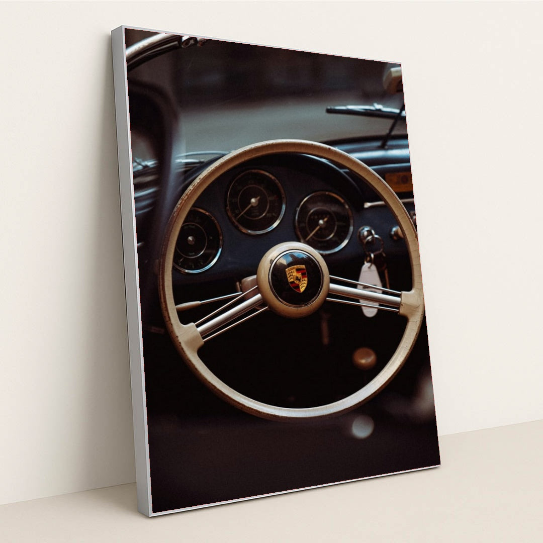 This photo shows the vintage steering wheel and gauges of a classic Porsche car, in a silver frame.