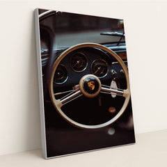 This photo shows the vintage steering wheel and gauges of a classic Porsche car, in a silver frame.