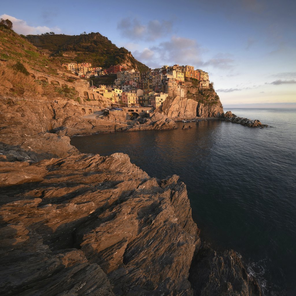 Paolo Razzauti - Breathtaking view of Manarola village perched on rugged cliffs at sunset, showcasing vibrant architecture and serene ocean.