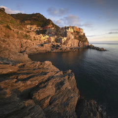 Paolo Razzauti - Breathtaking view of Manarola village perched on rugged cliffs at sunset, showcasing vibrant architecture and serene ocean.