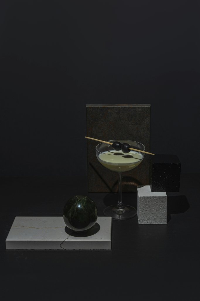 Mikhail Nilov - A geometric still life featuring a martini with olives against a dark background.