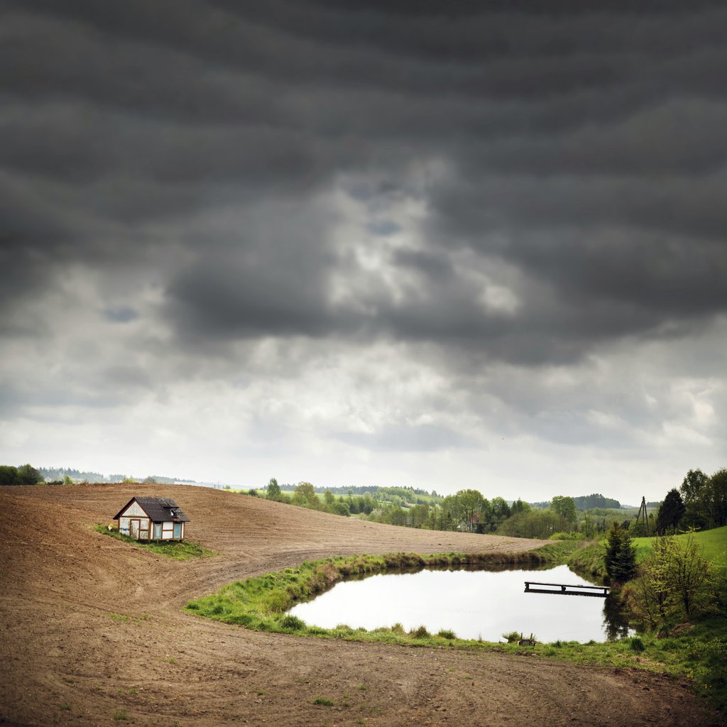 Piotr Arnoldes - Idyllic rural scene with cottage, pond, and dramatic sky in Szymbark, Poland.