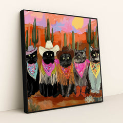 This artwork shows five cats in cowboy hats, bandanas, and boots posing in a colorful desert sunset scene with cacti, in a black frame.