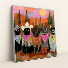This artwork shows five cats in cowboy hats, bandanas, and boots posing in a colorful desert sunset scene with cacti, in a silver frame.
