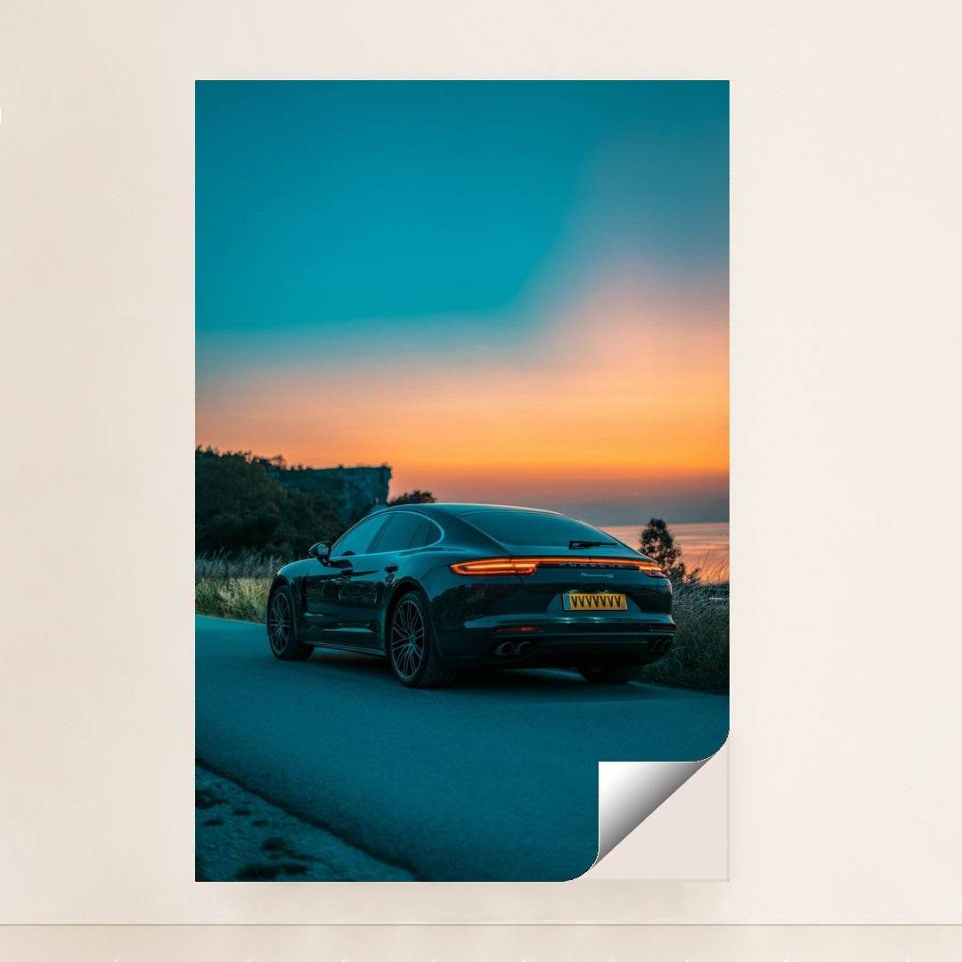This photo shows the rear side of a dark Porsche Panamera 4S sedan parked on a road overlooking a colorful sunset, minimalist unframed style.