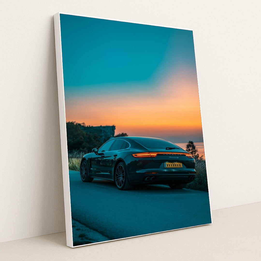 This photo shows the rear side of a dark Porsche Panamera 4S sedan parked on a road overlooking a colorful sunset, in a white frame.