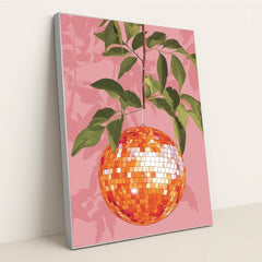 This artwork shows an orange disco ball hanging from a leafy branch against a pink background, in a silver frame.