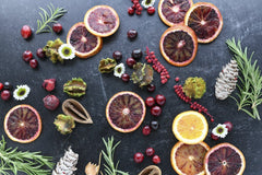 Heather Brock - A festive flat lay features blood oranges, pine cones, rosemary, and cranberries on a dark background.