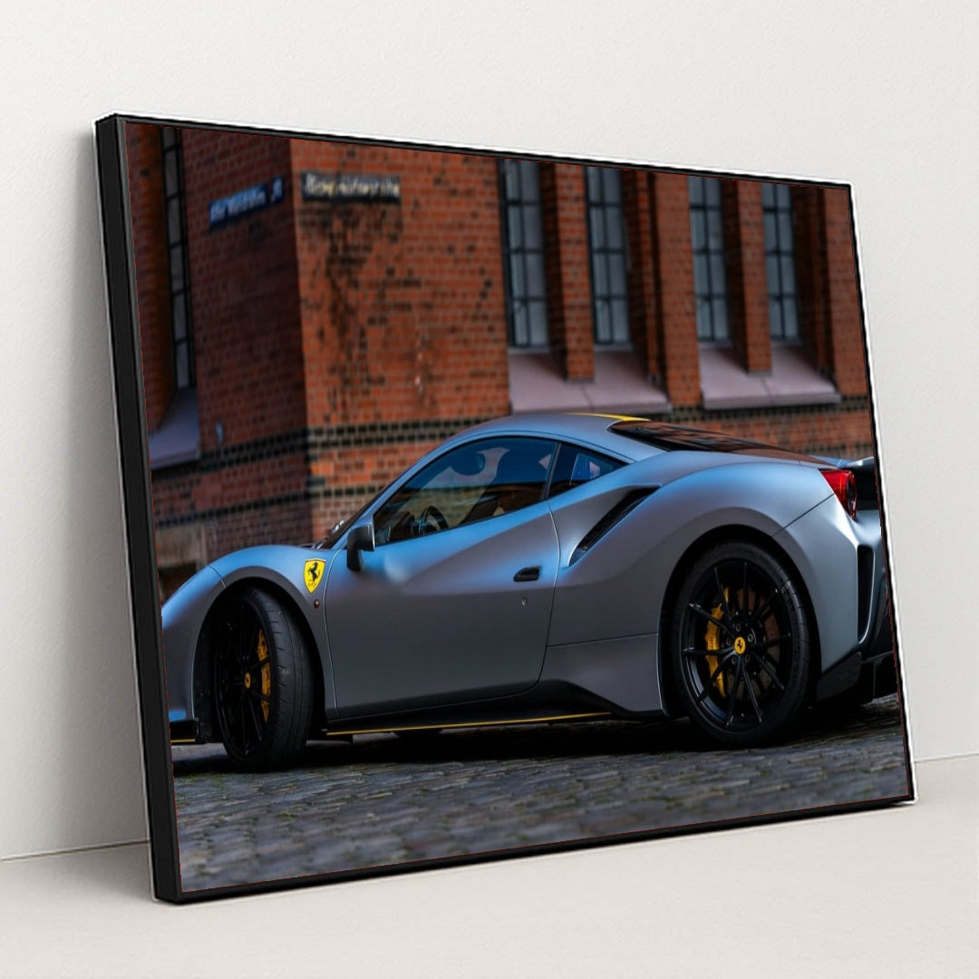 This photo shows a matte grey Ferrari 488 Pista with black wheels and yellow calipers parked by a brick building, in a black frame.