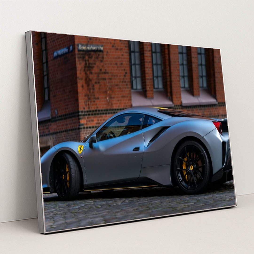 This photo shows a matte grey Ferrari 488 Pista with black wheels and yellow calipers parked by a brick building, in a silver frame.