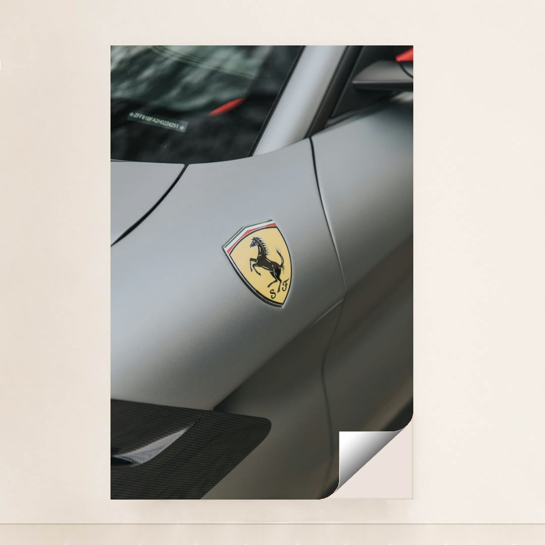 This photo shows a close-up of the Ferrari prancing horse badge on the fender of a matte gray Ferrari, minimalist unframed style.