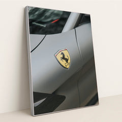 This photo shows a close-up of the Ferrari prancing horse badge on the fender of a matte gray Ferrari, in a silver frame.