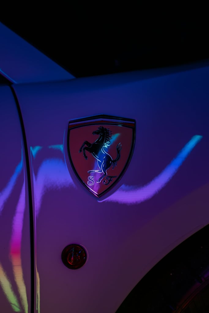 Ferrari Emblem Under Neon Lights, illuminated badge with vibrant reflections, showcasing car wall art aesthetics.