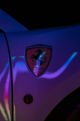 Ferrari Emblem Under Neon Lights, illuminated badge with vibrant reflections, showcasing car wall art aesthetics.