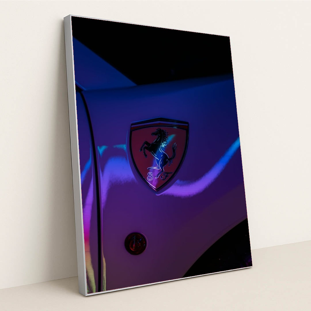 This photo shows a Ferrari prancing horse badge on a car fender illuminated with neon light reflections, in a silver frame.