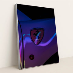 This photo shows a Ferrari prancing horse badge on a car fender illuminated with neon light reflections, in a silver frame.