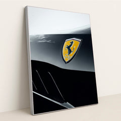 This photo shows a close-up of a Ferrari badge on a two-tone black and silver body panel, in a silver frame.