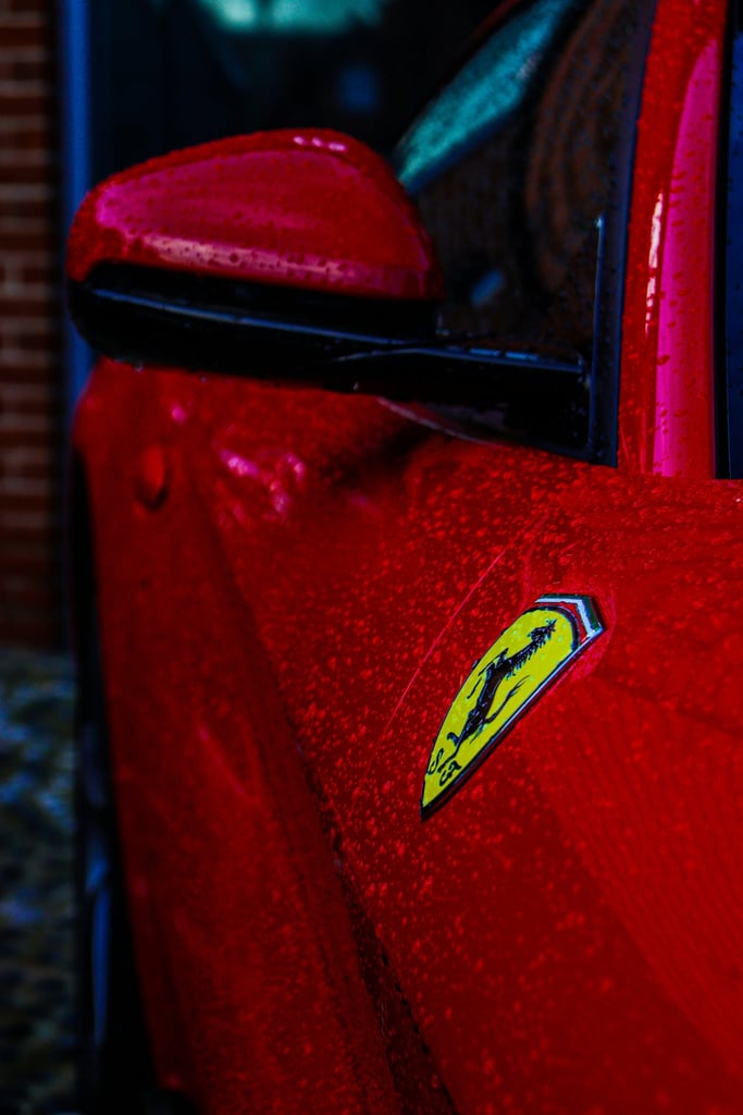 Close-up of a Ferrari in the Rain highlighting its red paint and yellow shield, perfect for car wall art.