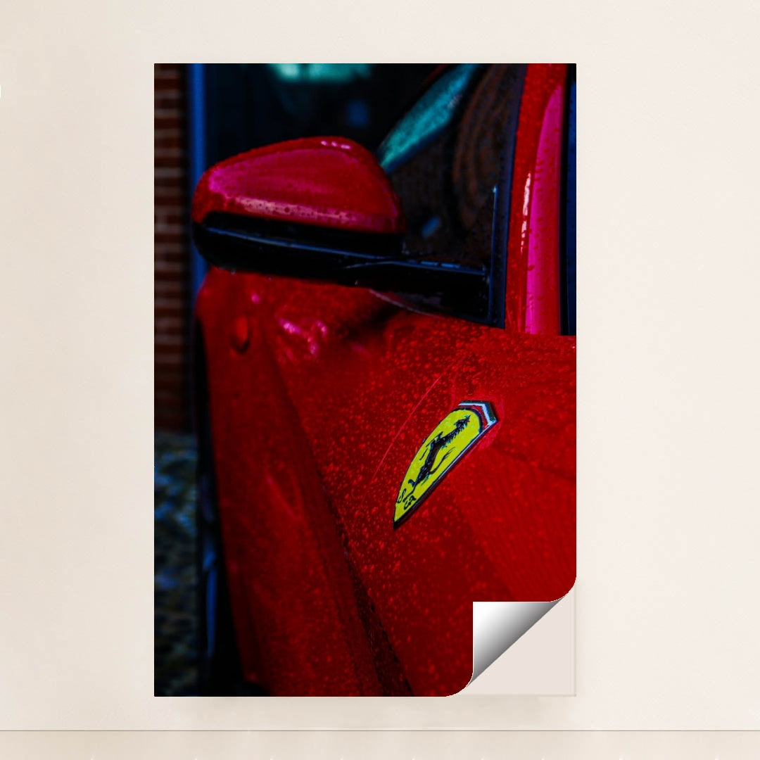 This photo shows the close-up of a red Ferrari’s fender and badge covered in rain droplets, minimalist unframed style.