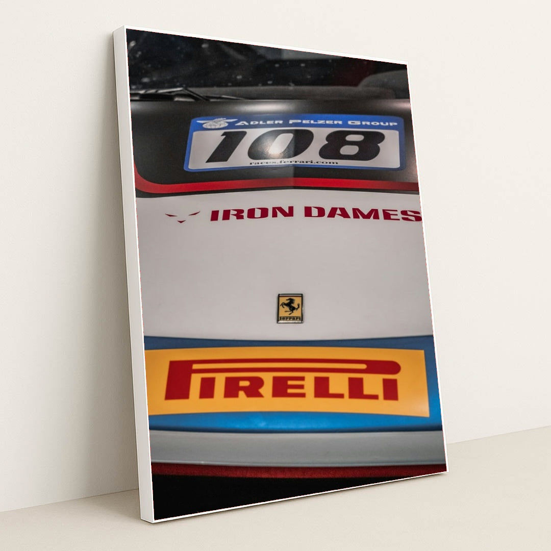 This photo shows a close-up of the hood of a Ferrari race car with Iron Dames and Pirelli logos, in a white frame.