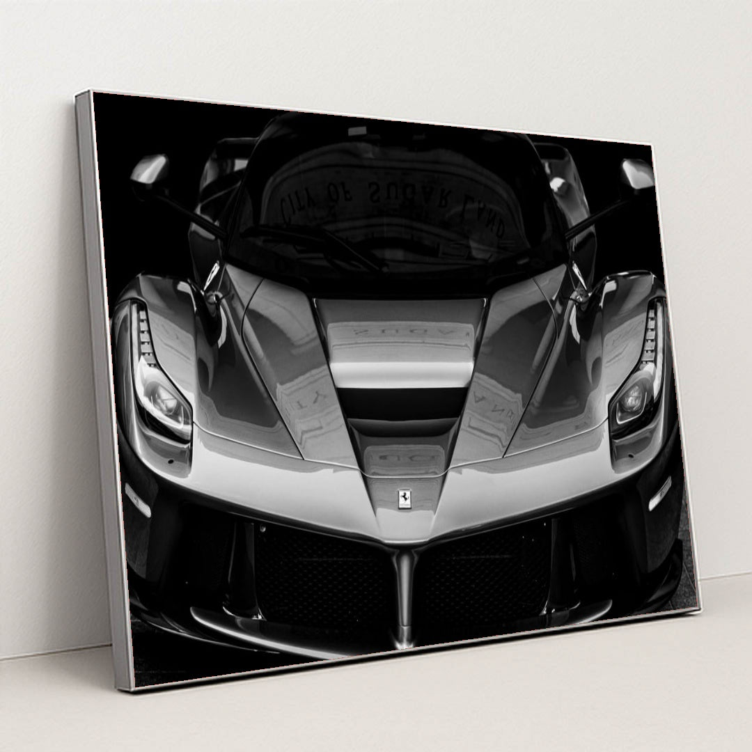 This photo shows the front view of a Ferrari hypercar in dramatic black and white, in a silver frame.
