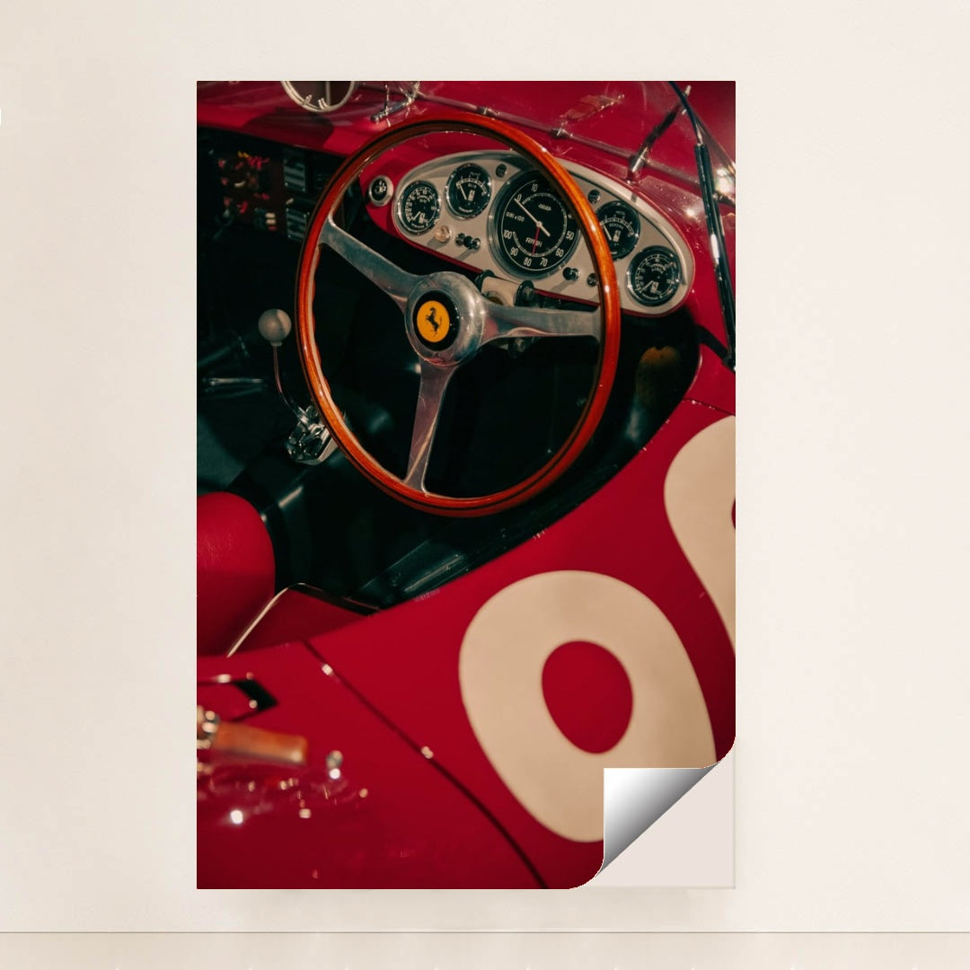 This photo shows the cockpit of a classic red Ferrari race car with a wooden steering wheel and vintage gauges, unframed style.
