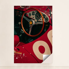 This photo shows the cockpit of a classic red Ferrari race car with a wooden steering wheel and vintage gauges, unframed style.
