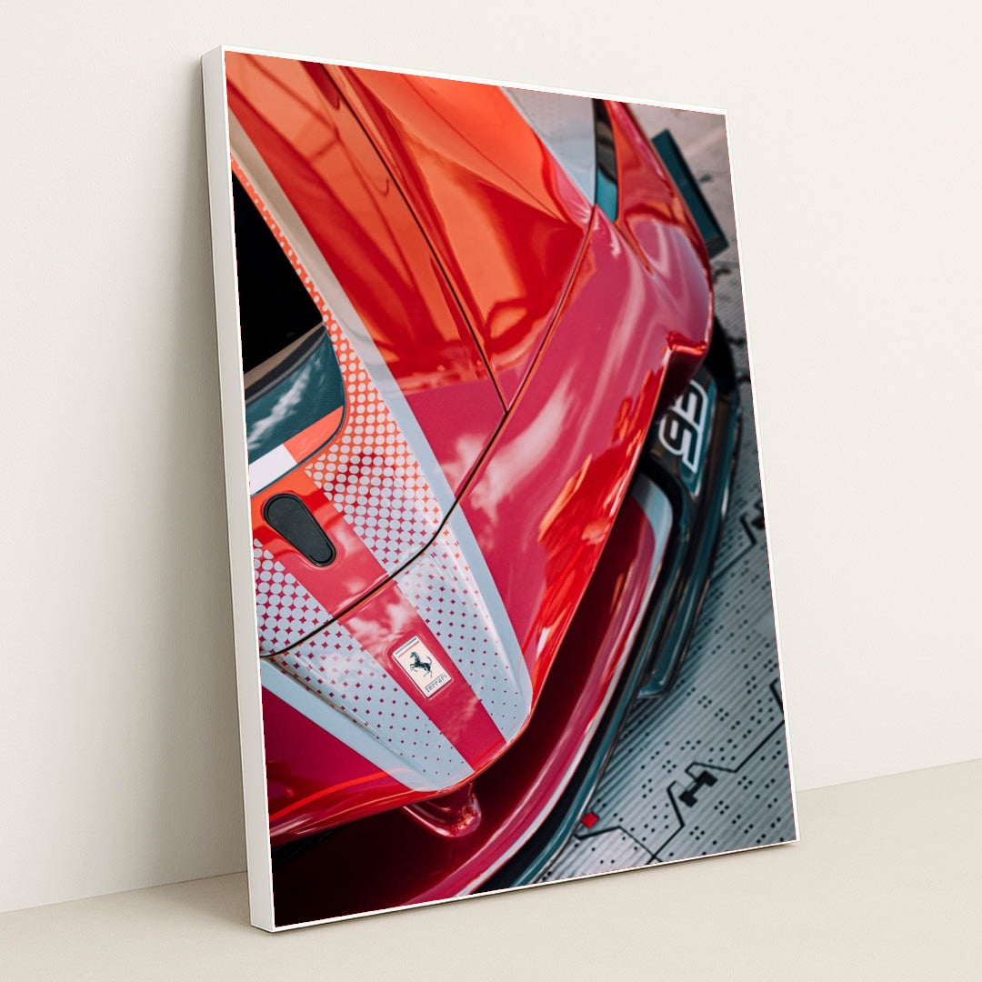 This photo shows a close-up view of a red Ferrari with dotted racing stripes reflecting dramatic skies, in a white frame.