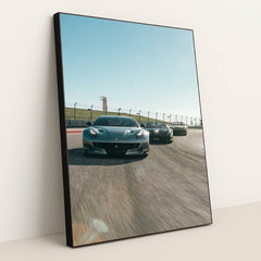 This photo shows three grey Ferrari sports cars racing side by side on a sunny racetrack, in a black frame.