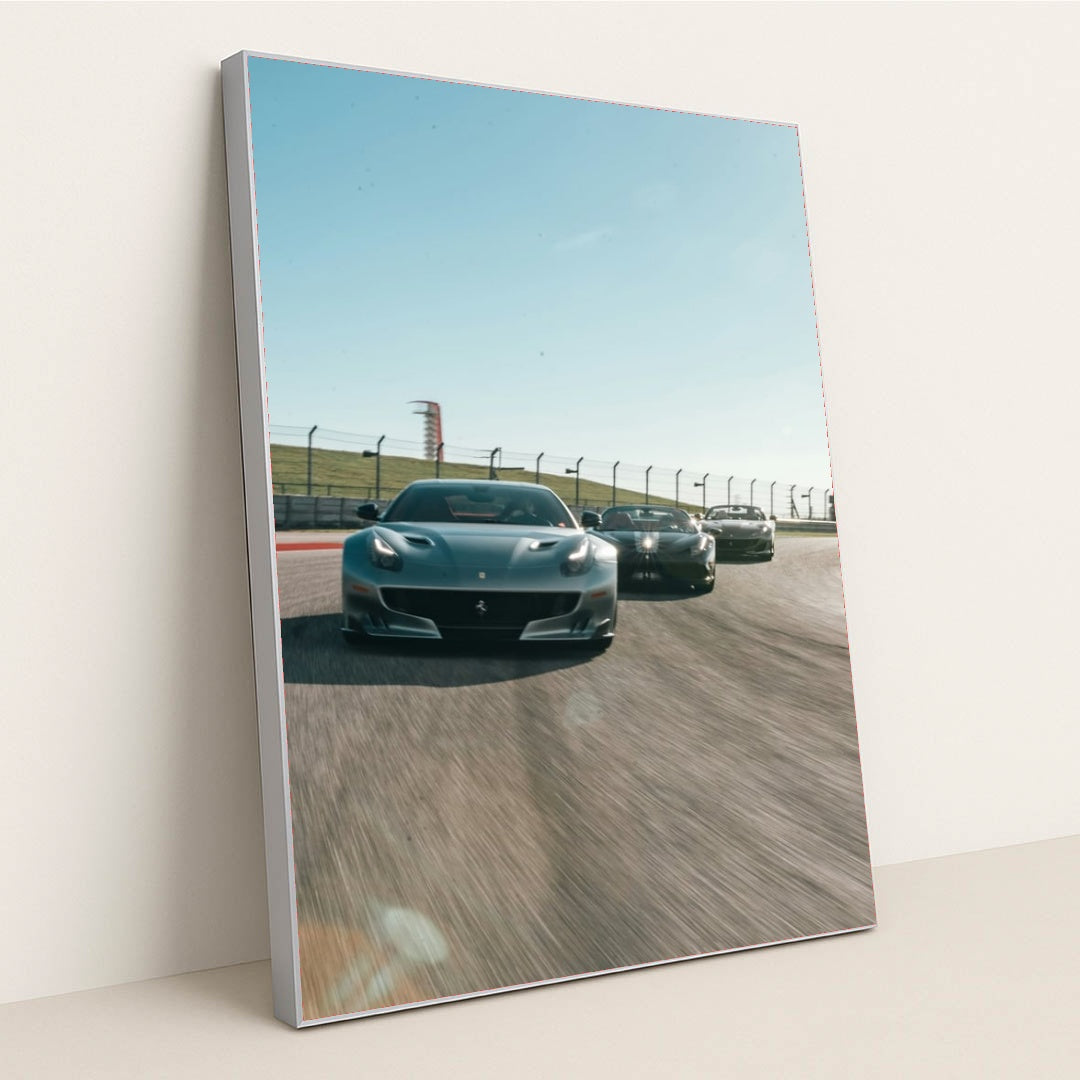 This photo shows three grey Ferrari sports cars racing side by side on a sunny racetrack, in a silver frame.