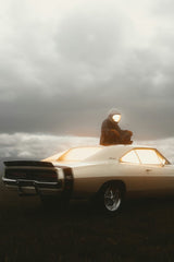 Astronaut sitting on vintage Dodge Charger glowing from within, cloudy sky; a unique car wall art titled Golden Glow.