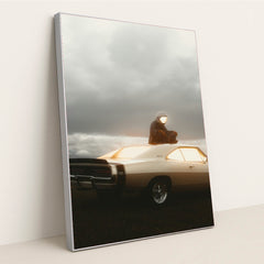 This photo shows a person in an astronaut suit sitting on the roof of a classic Dodge Charger at dusk, in a silver frame.