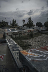 Connor McManus - A moody urban skatepark scene featuring graffiti-covered structures under an overcast sky.