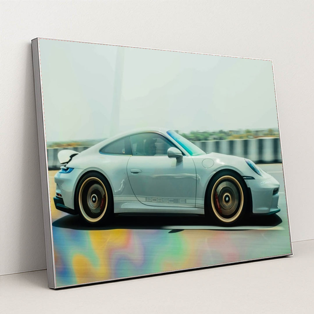 This photo shows a silver Porsche sports car in motion on a highway with colorful reflections on the road, in a silver frame.