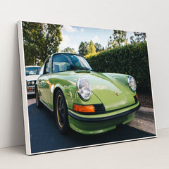 This photo shows a classic Porsche 911 in light green parked on a sunny street with trees in the background, in a white frame.