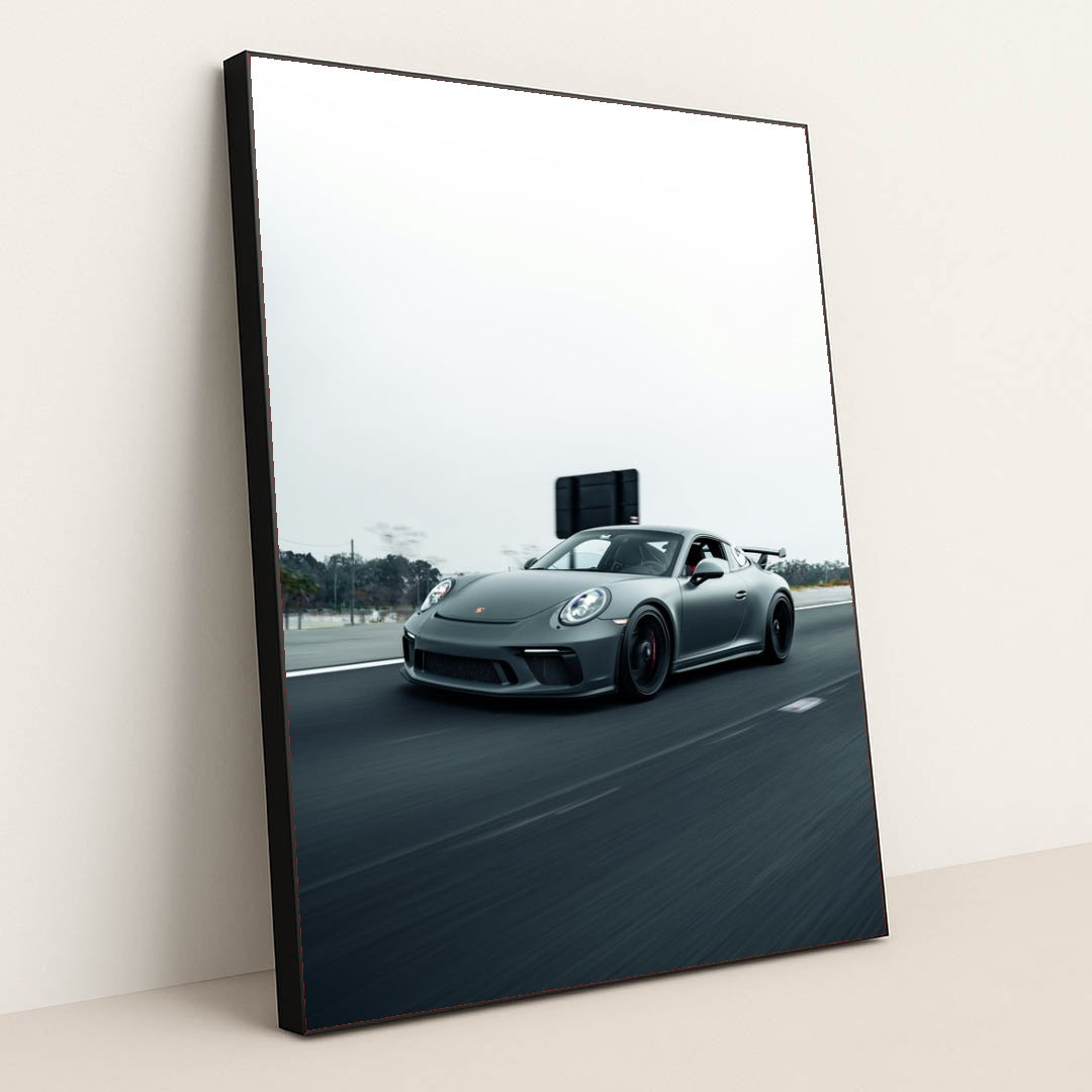 This photo shows a gray Porsche sports car driving fast on a highway with a blurred background, in a black frame.