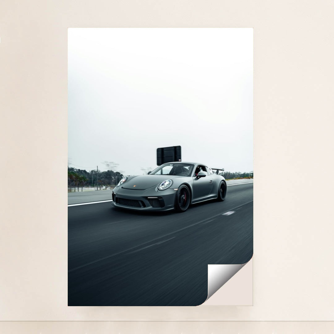 This photo shows a gray Porsche sports car driving fast on a highway with a blurred background, unframed.
