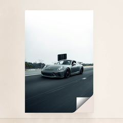 This photo shows a gray Porsche sports car driving fast on a highway with a blurred background, unframed.