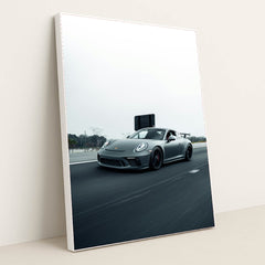 This photo shows a gray Porsche sports car driving fast on a highway with a blurred background, in a white frame.