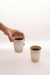 Cup of Couple - A minimalist photo of two disposable coffee cups, one held by a hand, against a plain background.