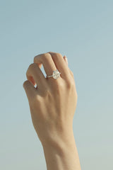 hana mori - A close-up of a hand wearing a diamond ring against a clear blue sky, showcasing elegance and simplicity.