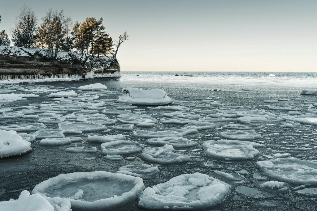 Raul Ling - A serene winter landscape featuring a frozen lake with unique ice formations near a wooded shoreline.