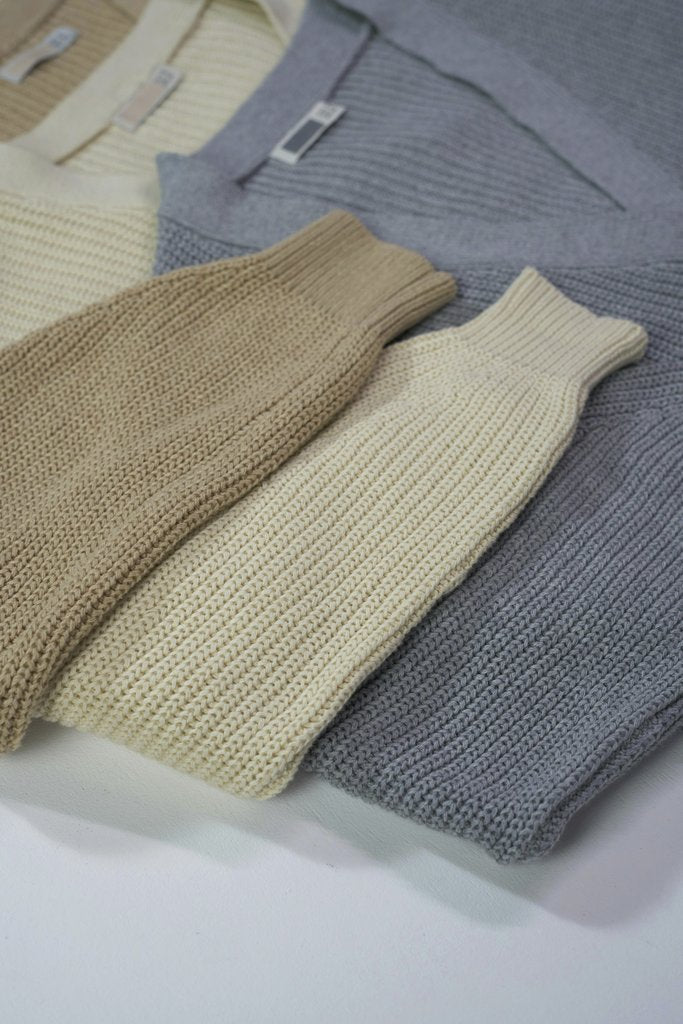 Ron Lach - A collection of folded knit sweaters in earthy tones displayed in a flat lay arrangement.