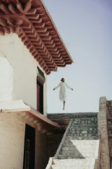 Mehdi El Marouazi - A person leaps in joy near traditional Moroccan architecture in a serene outdoor setting.