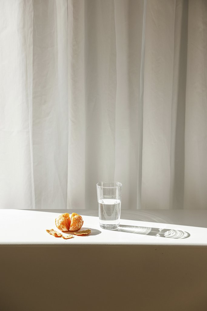 Cup of Couple - A peeled orange with a glass of water on a sunlit table, creating a minimalist still life scene.