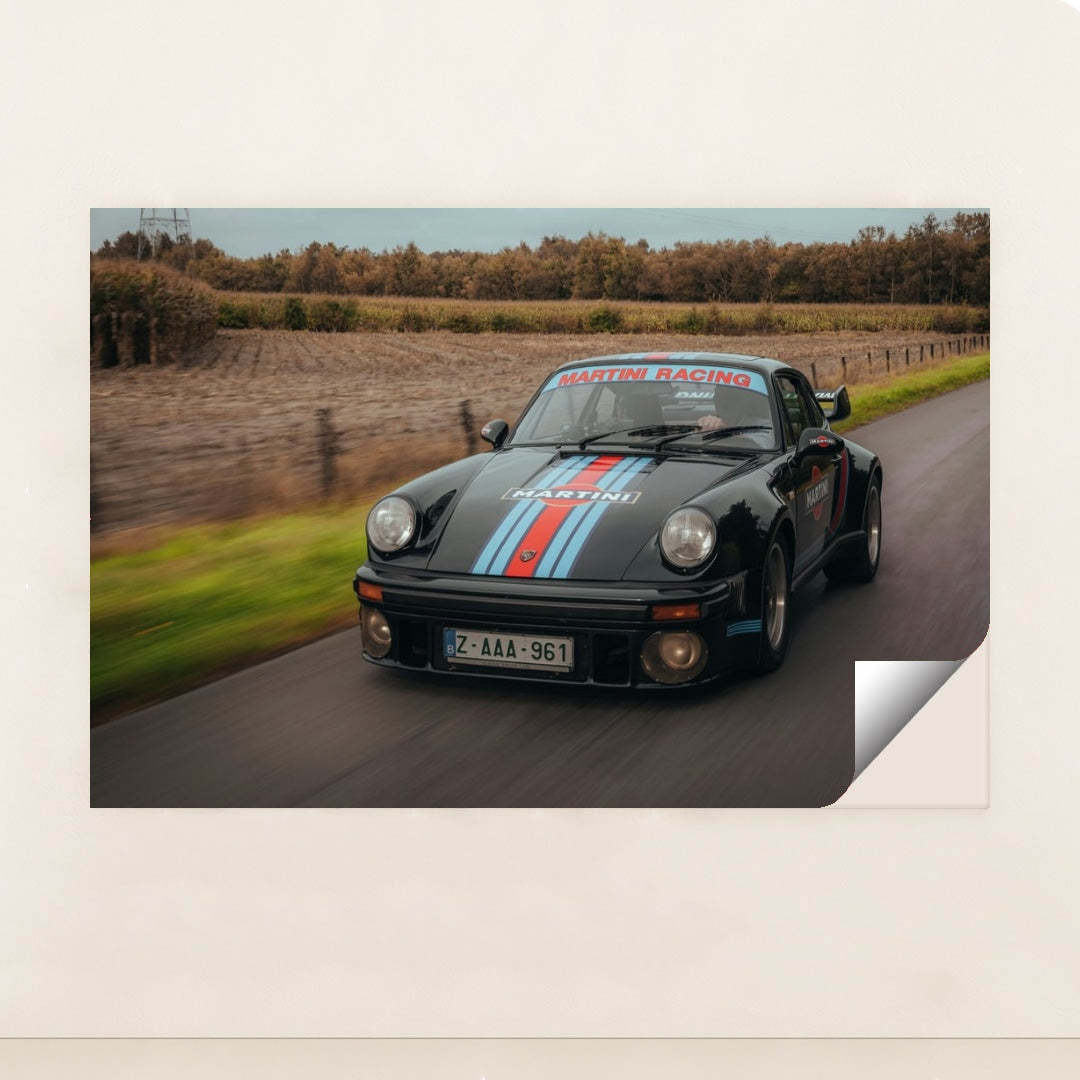 This photo features a vintage black Porsche with Martini Racing stripes driving on a rural road, unframed.