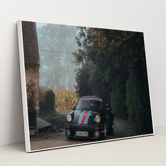 This photo shows a black Porsche with Martini Racing livery parked on a cobblestone driveway next to a brick house on a foggy morning, in a white frame.