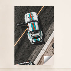 This photo shows an overhead view of a white Porsche race car with Martini stripes and an open door on a racetrack, unframed.